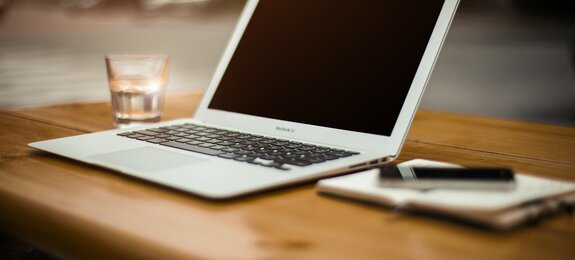 Laptop auf Tisch mit Glas, Block und Stift