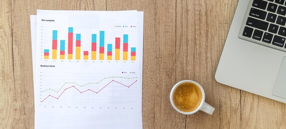 Diagramme auf Papier mit Kaffeetasse und Laptop