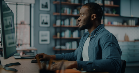 Handsome Black African American Specialist Working on Desktop Computer in Creative Home Living Room. Freelance Male is Working on a Finance Presentation Report for Clients and Employer