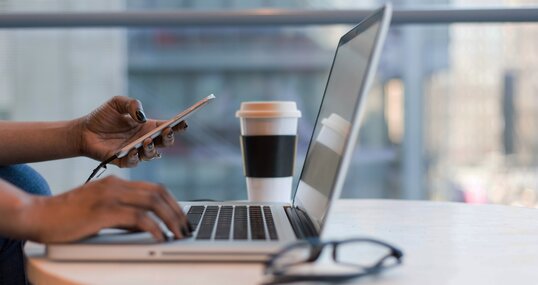 Frau arbeitet remote mit Smartphone und Laptop