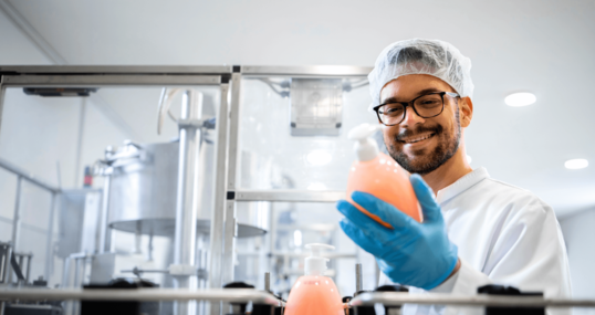 Production line worker or technologist in white sterile uniform working in chemical industry and checking quality of liquid soap or detergent in factory.