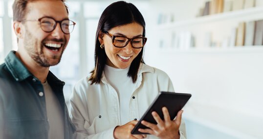 Female designer standing with her colleague and using a tablet