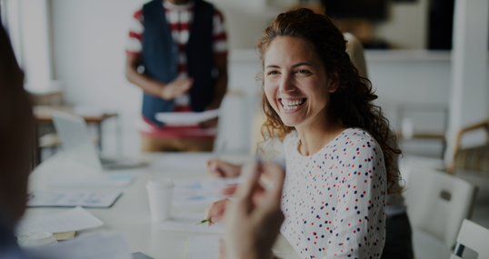 Happy young businesswoman sitting at desk and communicating with her colleagues during a meeting