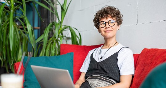 Happy young female in elegant casualwear sitting on couch with laptop in front