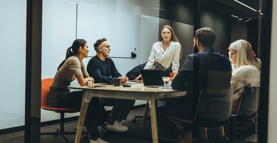 Eine Gruppe von Entwicklern und Entscheidern sitzt zusammen in einem modernen Meetingraum, um eine strategische Auditmanagement-Lösung zu finden.